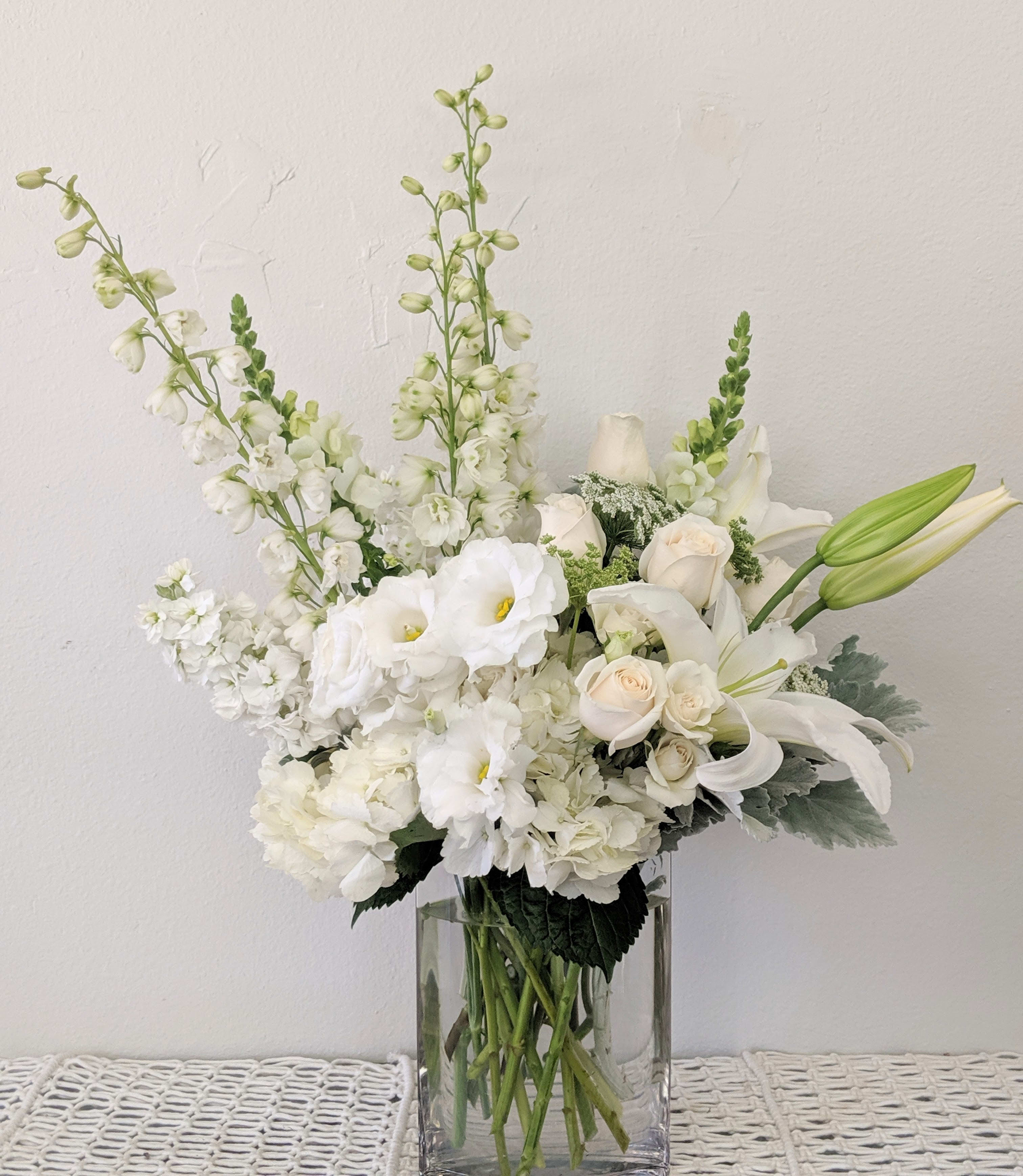White floral arrangement in a clear glass vase with lilies and roses