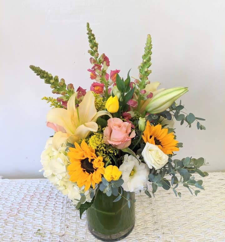 Mixed bouquet in a glass vase with sunflowers, lilies, roses, and tulips
