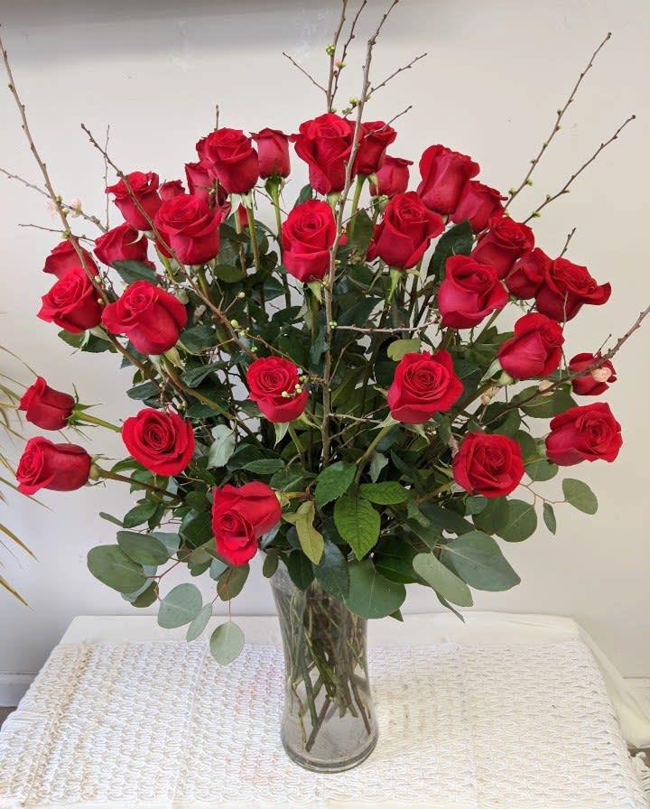 Red roses arranged in a clear glass vase with branching accents
