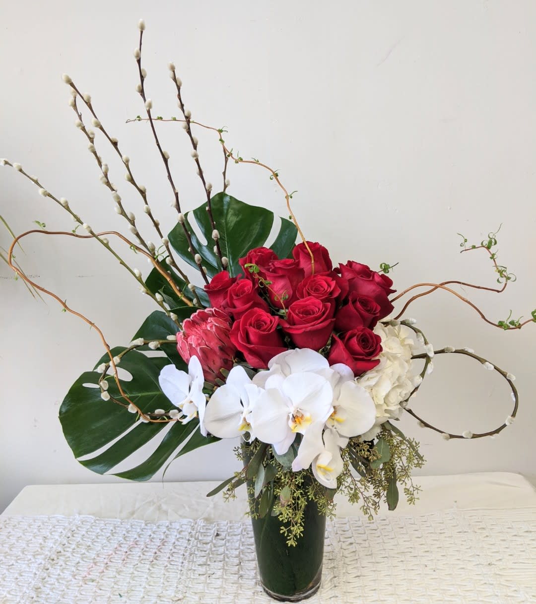 Red roses and white orchids in a tall vase with large leaves