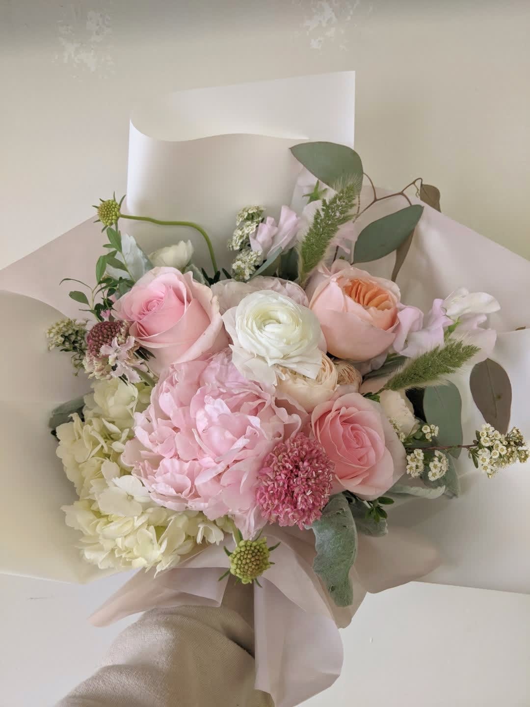Hand-tied bouquet of pink and white flowers wrapped in pale paper