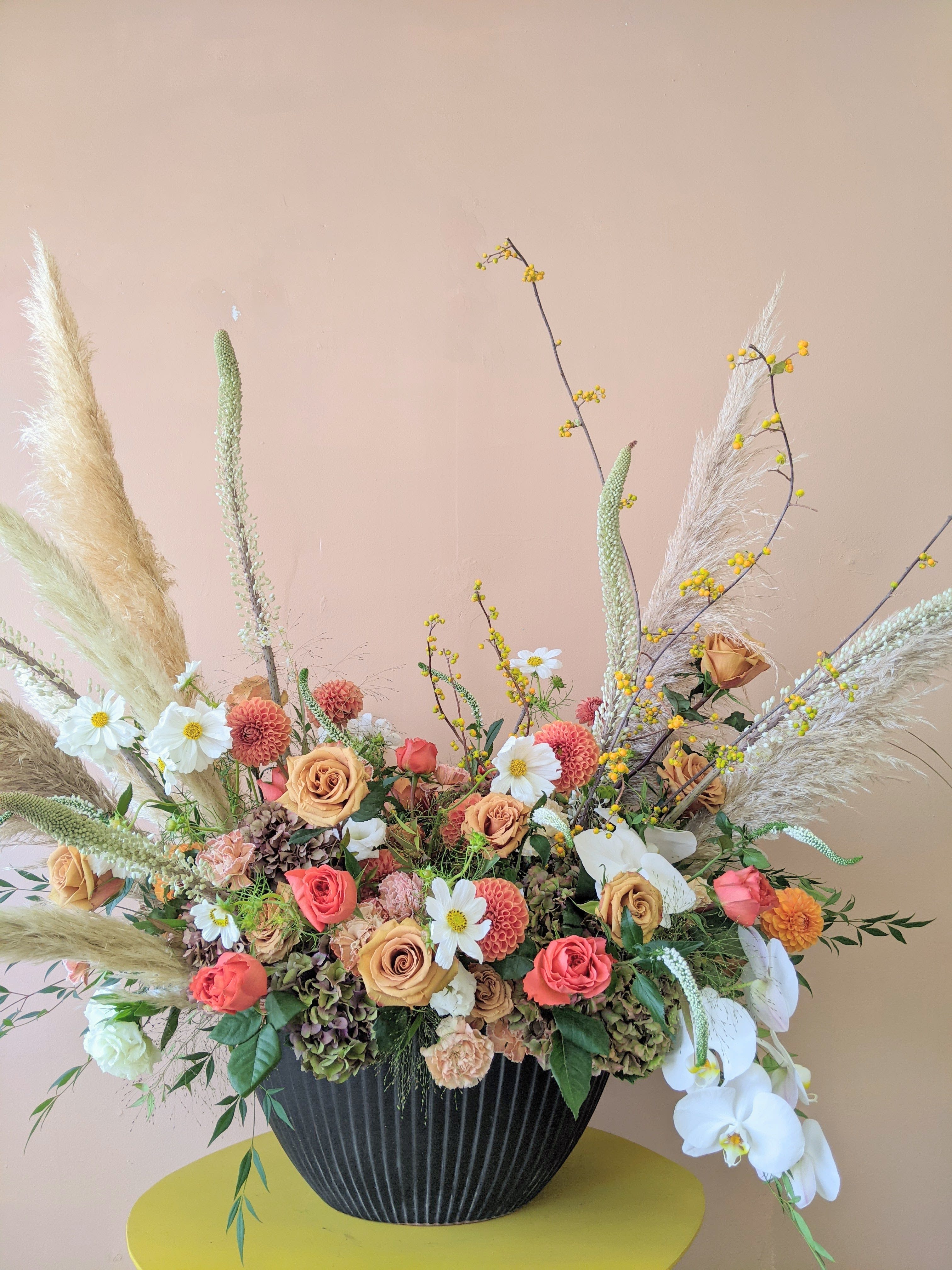 Large floral arrangement with peach roses, white orchids, and pampas grass in a black vase