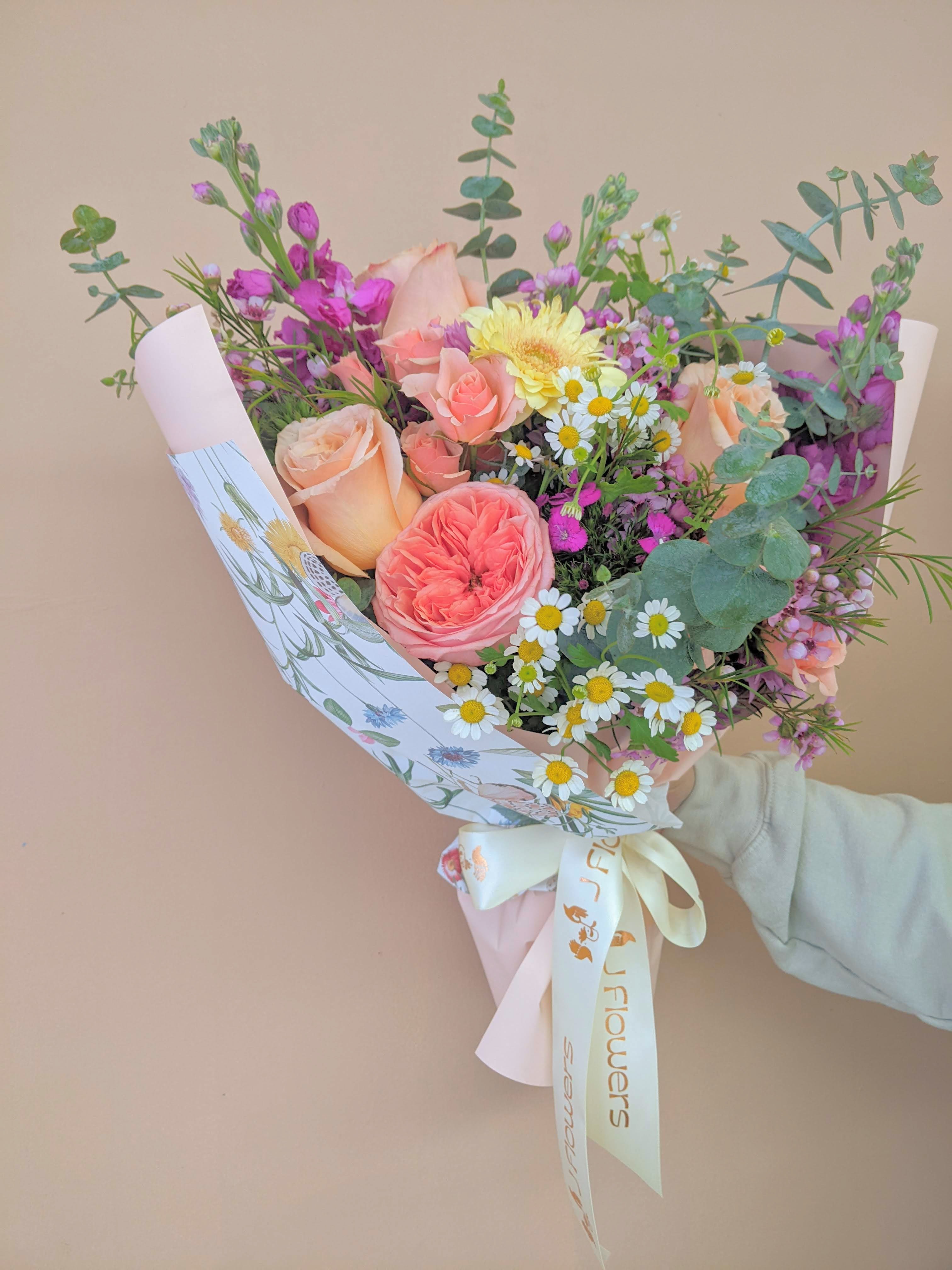 Hand-tied bouquet of peach and pink roses with small white daisies