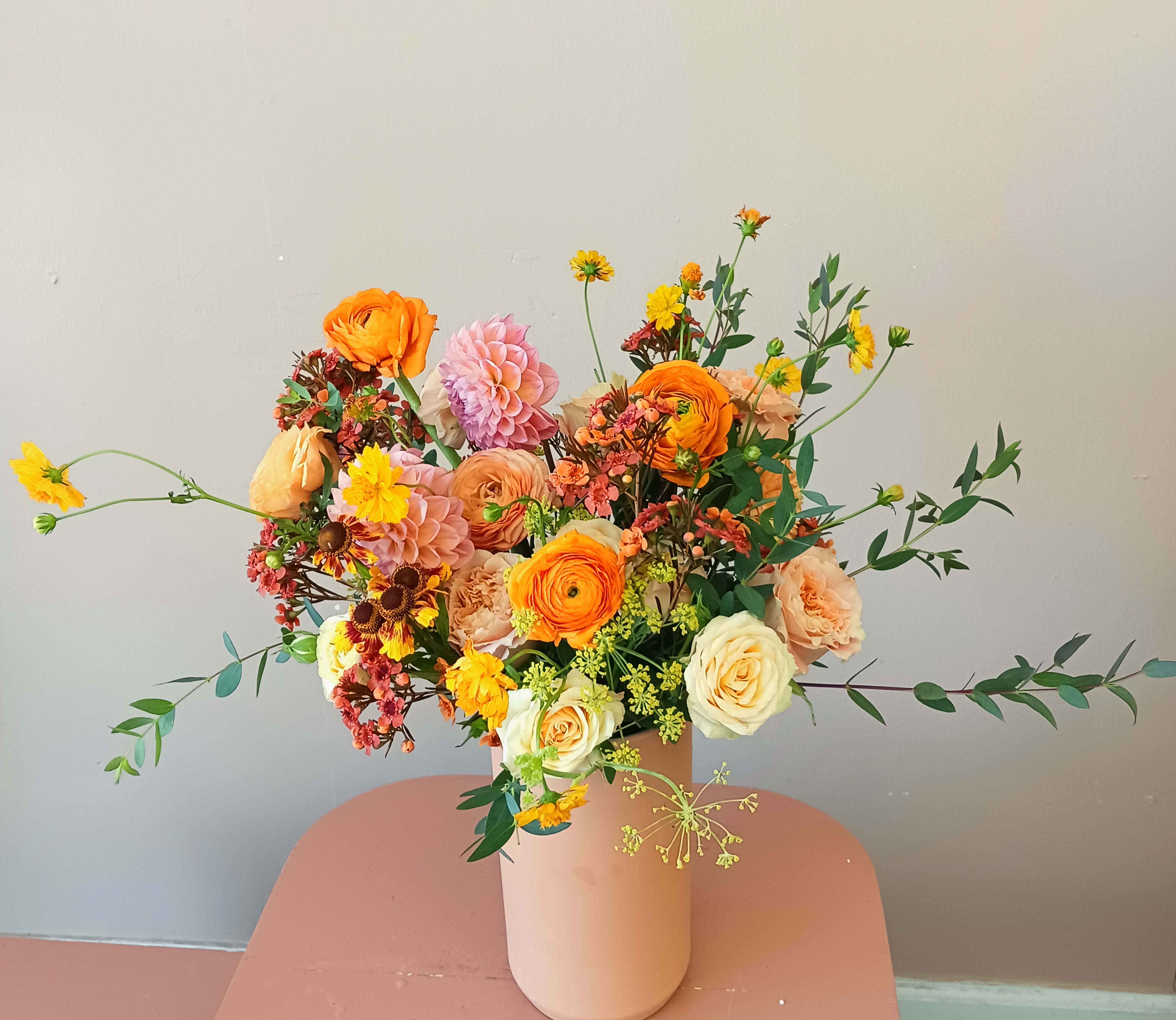 Mixed bouquet of orange, pink, and cream flowers in a blush vase