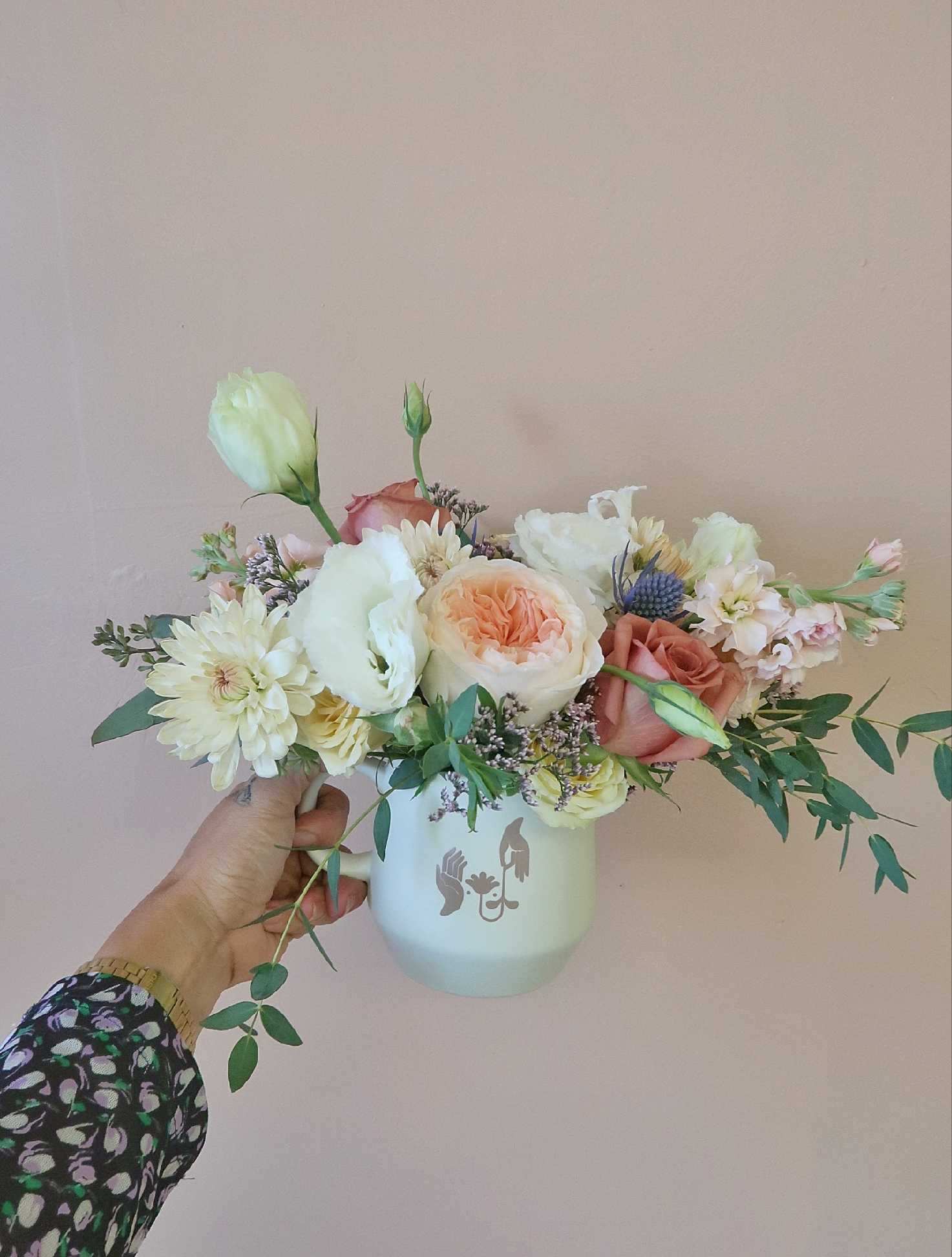 Handheld bouquet of pastel roses and white blooms in a white mug vase