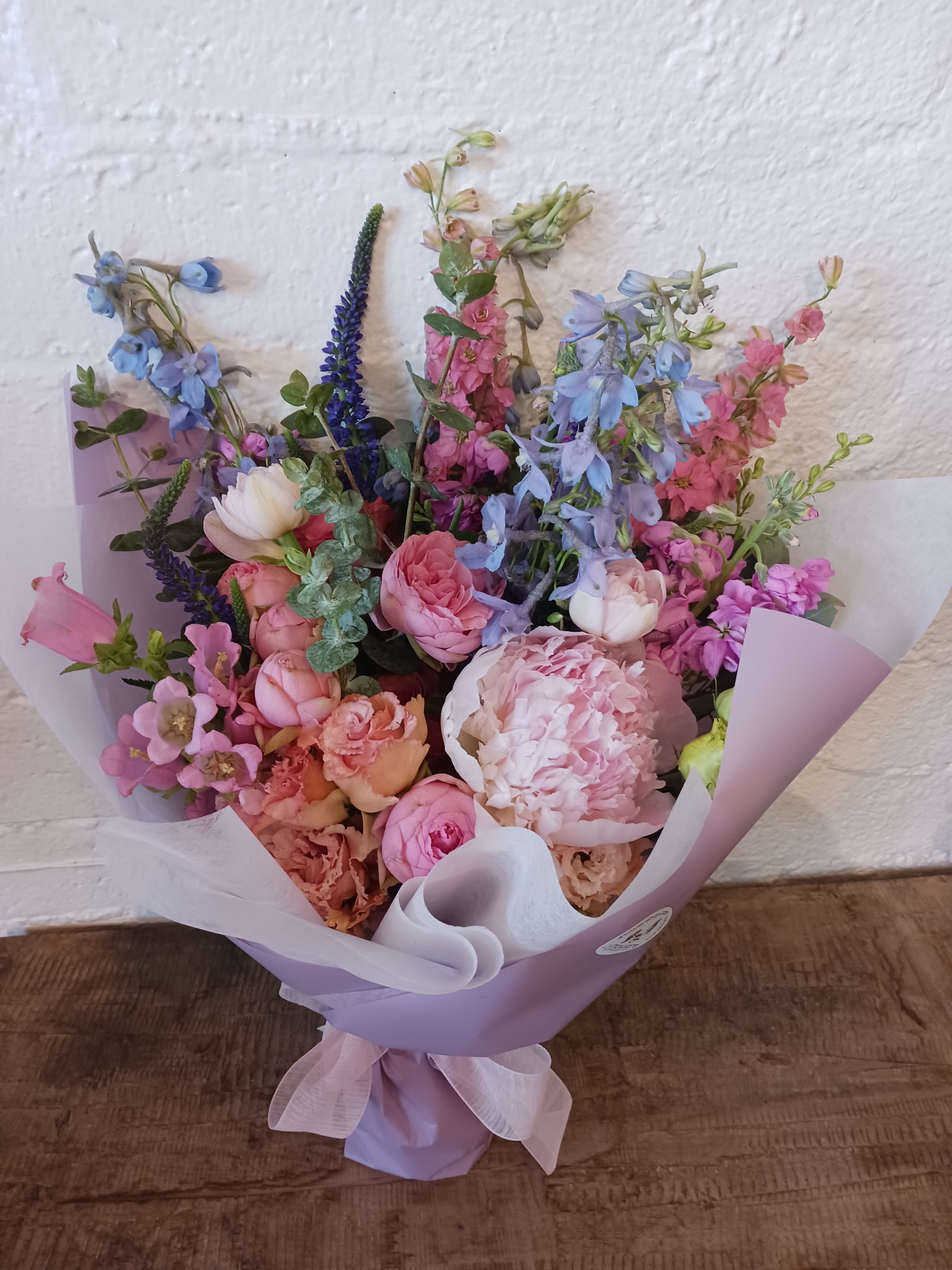 Pastel bouquet of pink, blue, and peach flowers wrapped in lavender paper