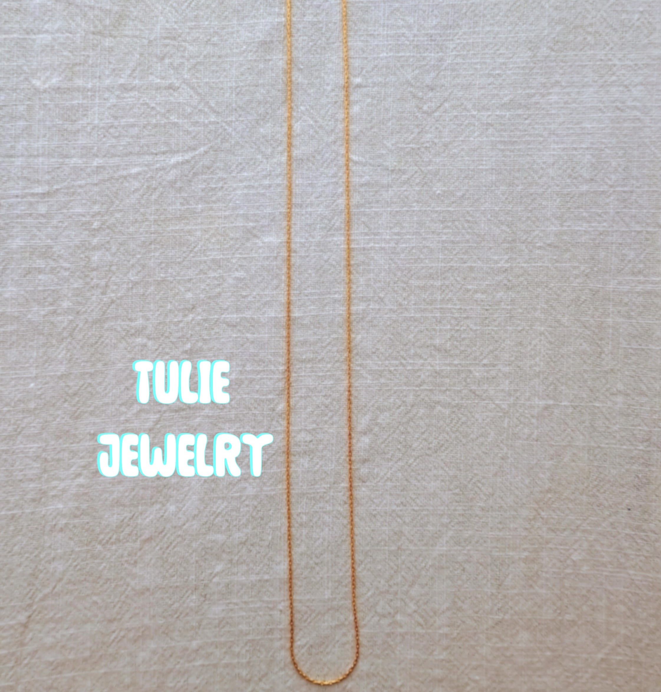 A thin gold necklace laid flat on a light fabric background.