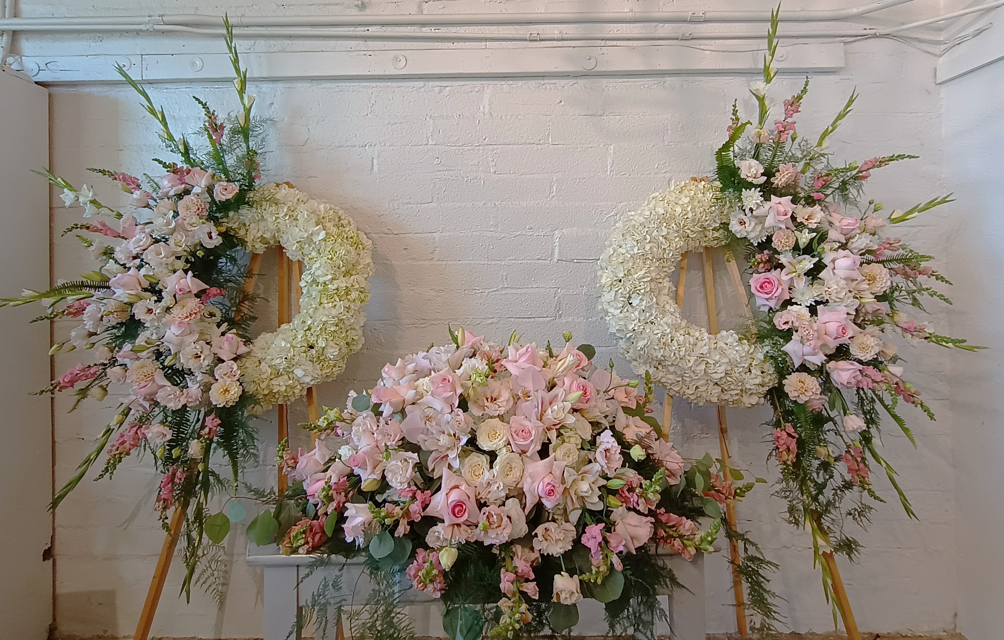 Three pastel floral wreaths and sprays on easels with a large pink centerpiece below.