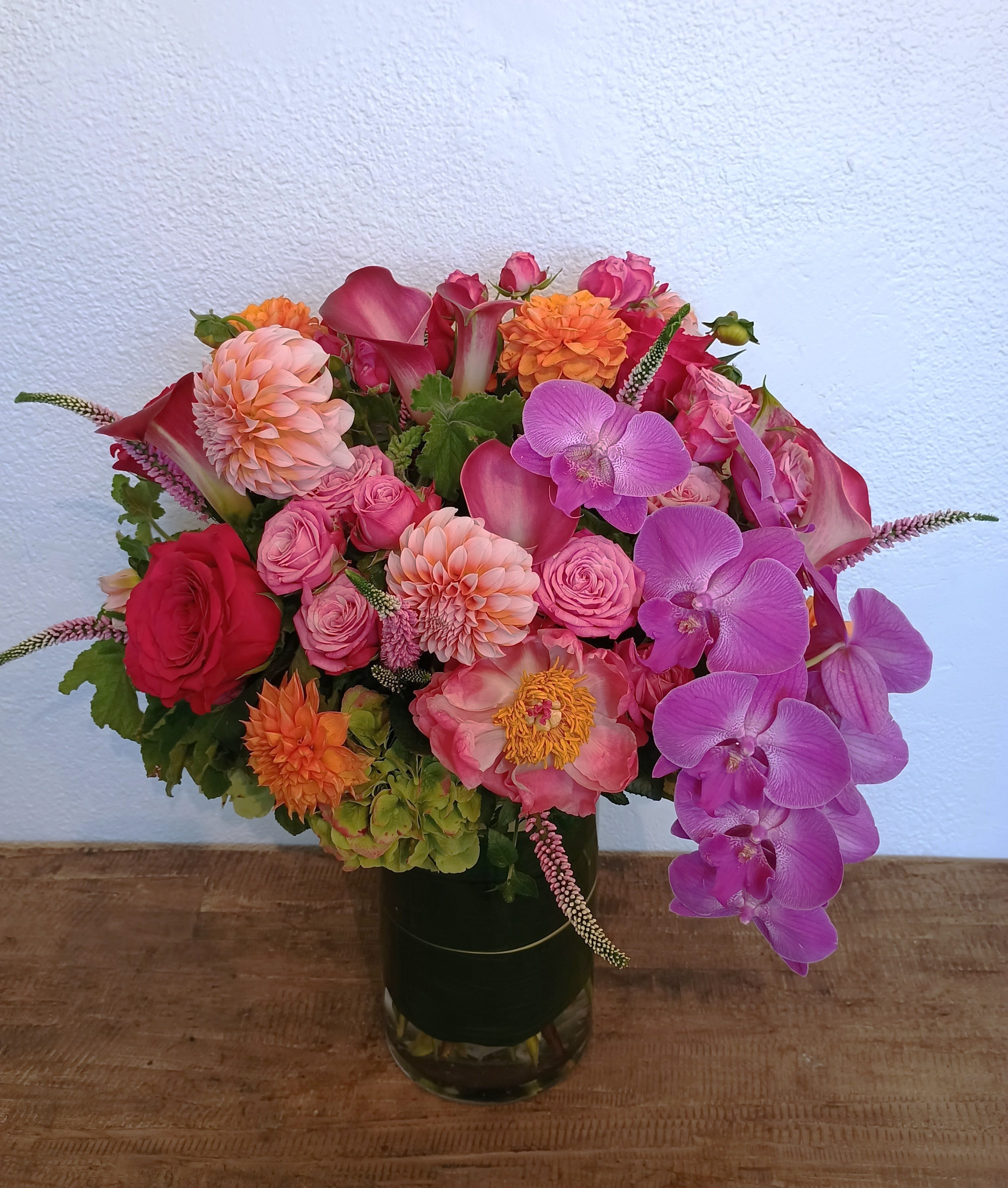 Colorful bouquet of roses, dahlias, calla lilies, and orchids in a glass vase