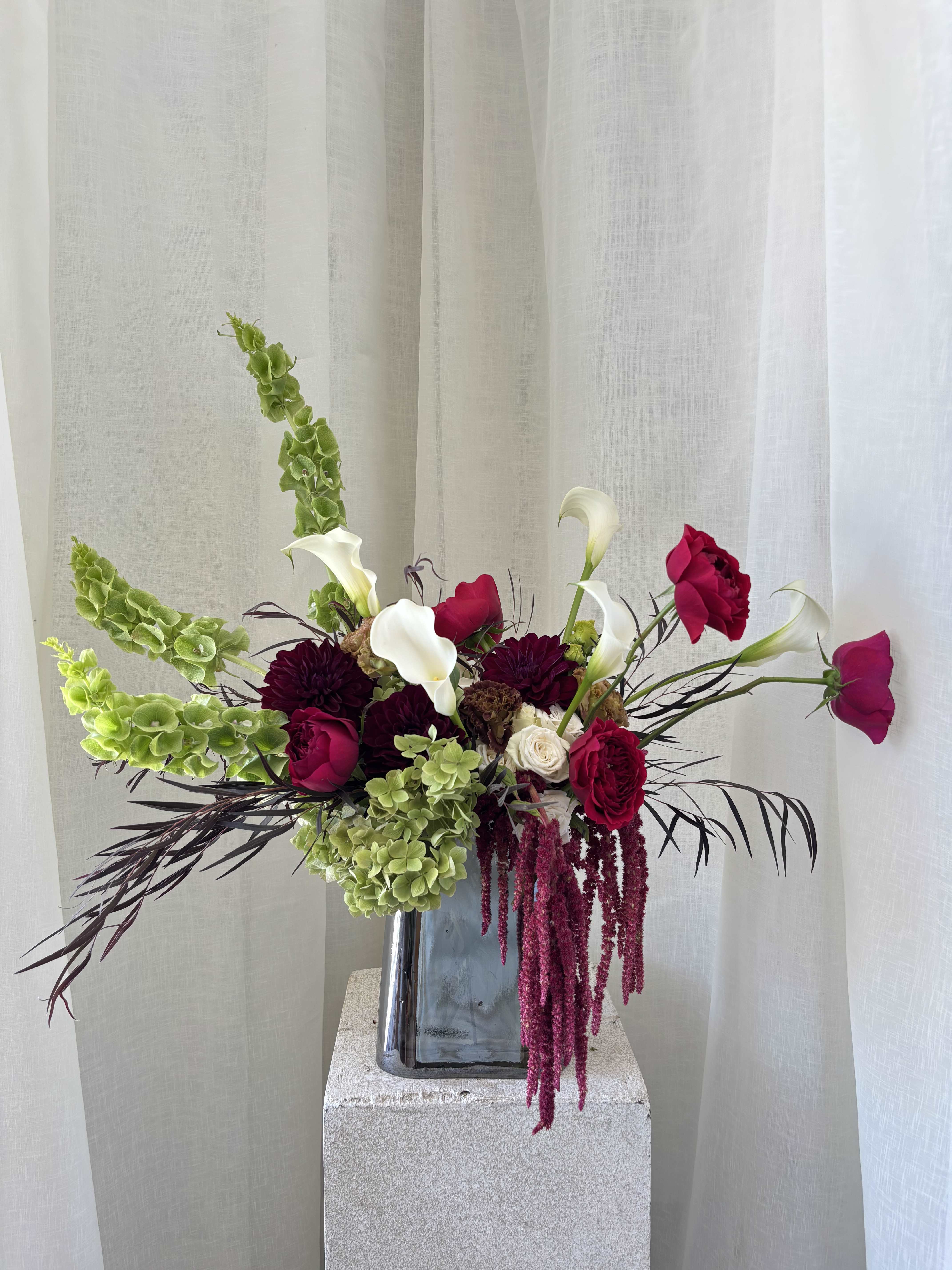 Tall floral arrangement with white calla lilies, magenta roses, and green hanging blooms in a vase.