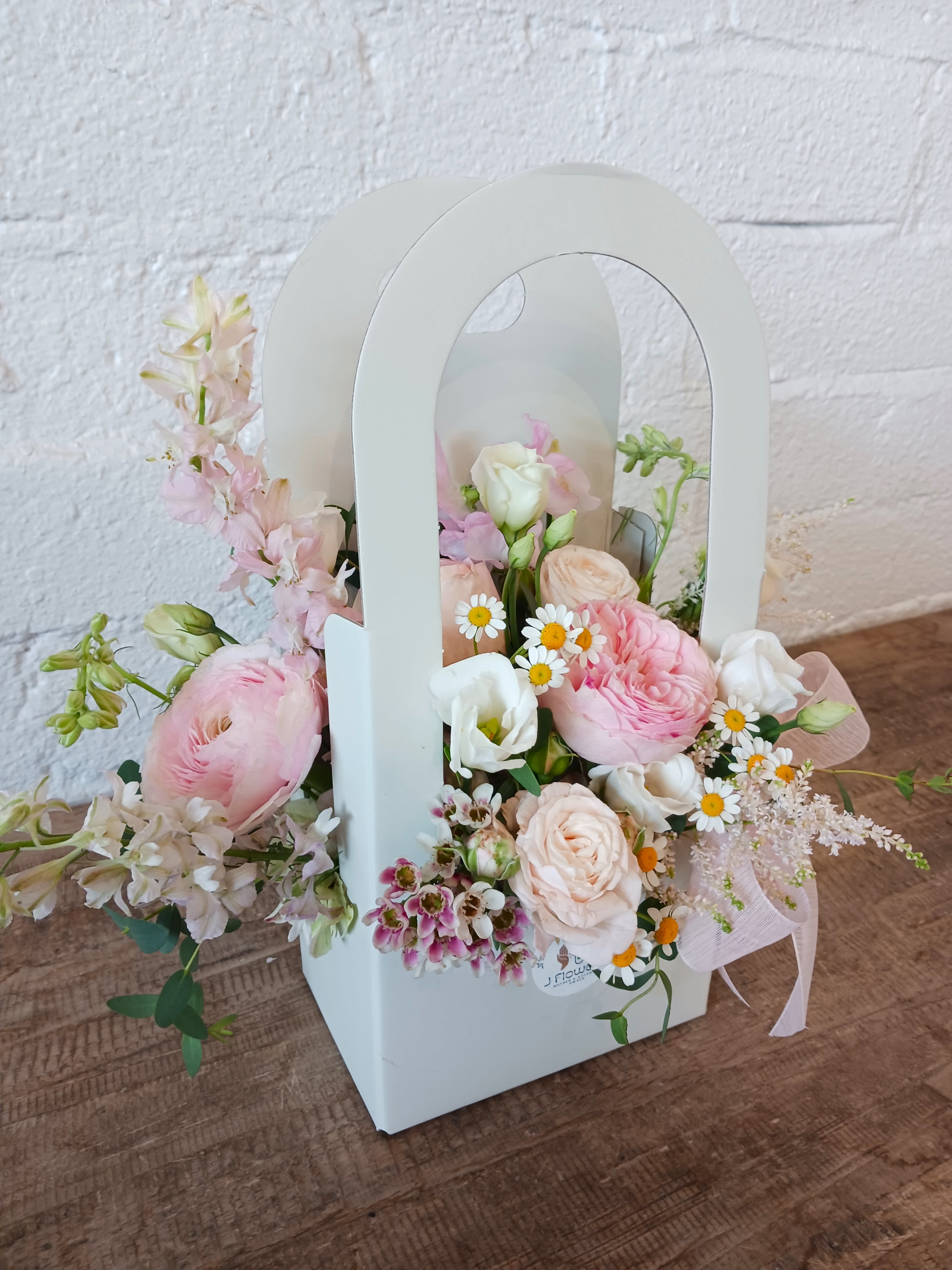 Pastel flower arrangement in a white handled box with pink and white blooms