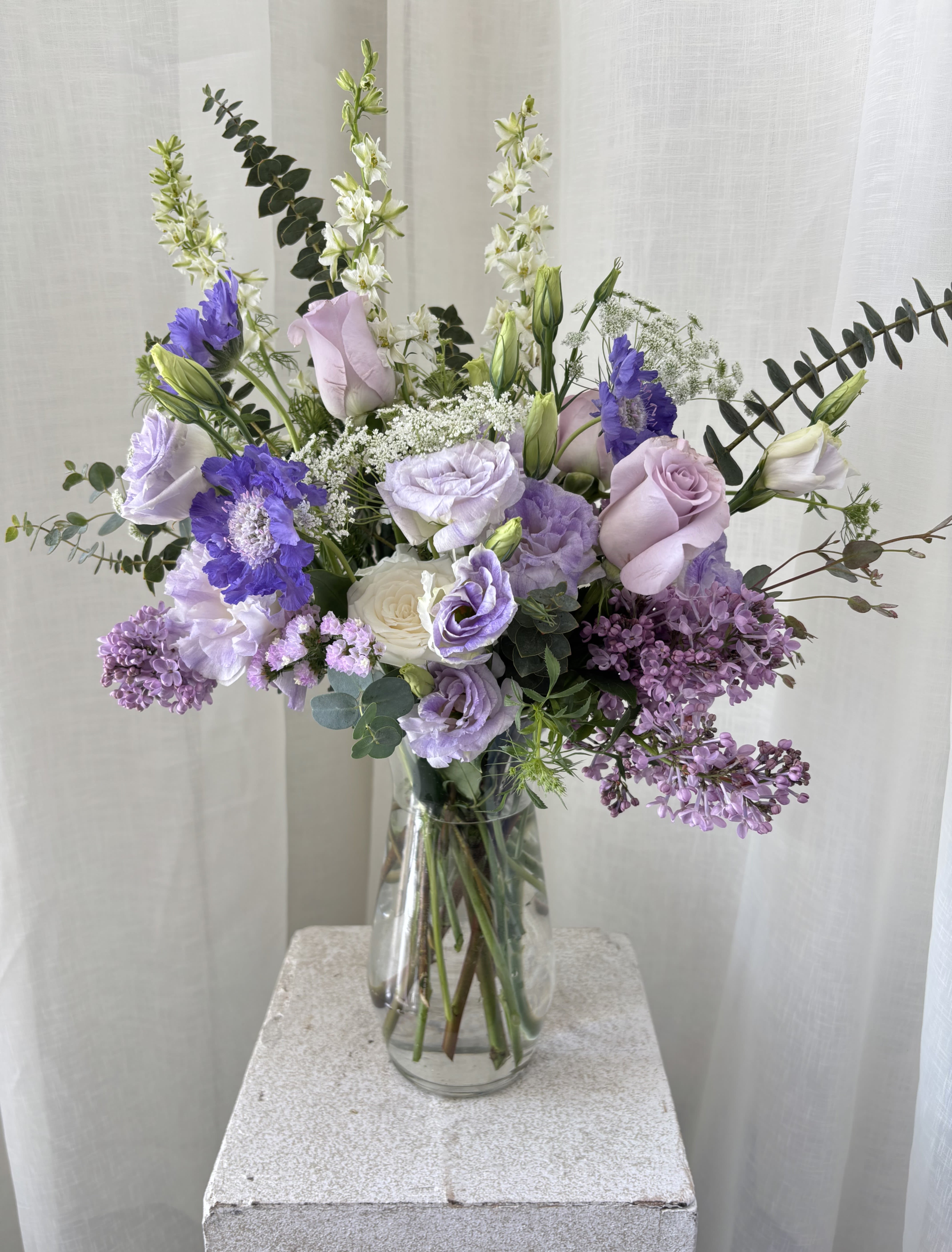 Tall lavender and white flower arrangement in a clear glass vase.