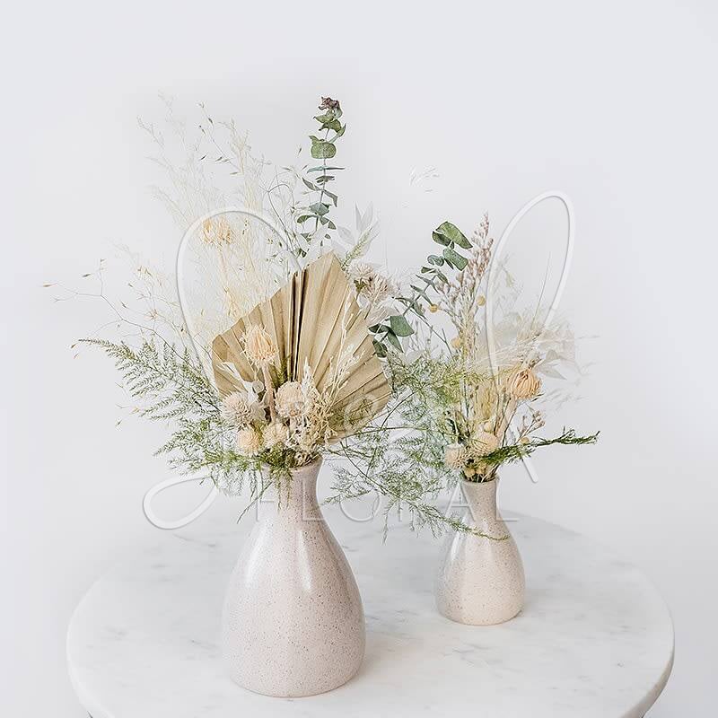 Two dried floral arrangements in cream vases on a round table