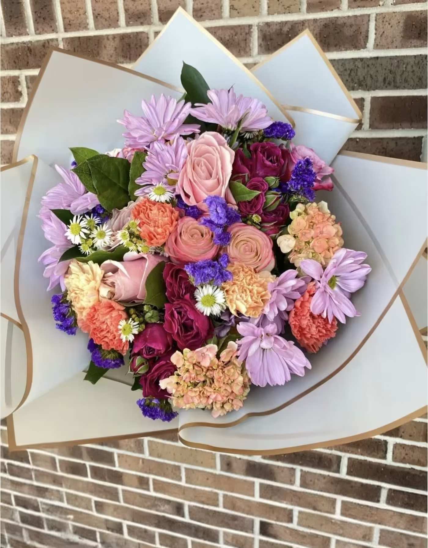 Mixed bouquet of pink, purple, and peach flowers wrapped in white paper