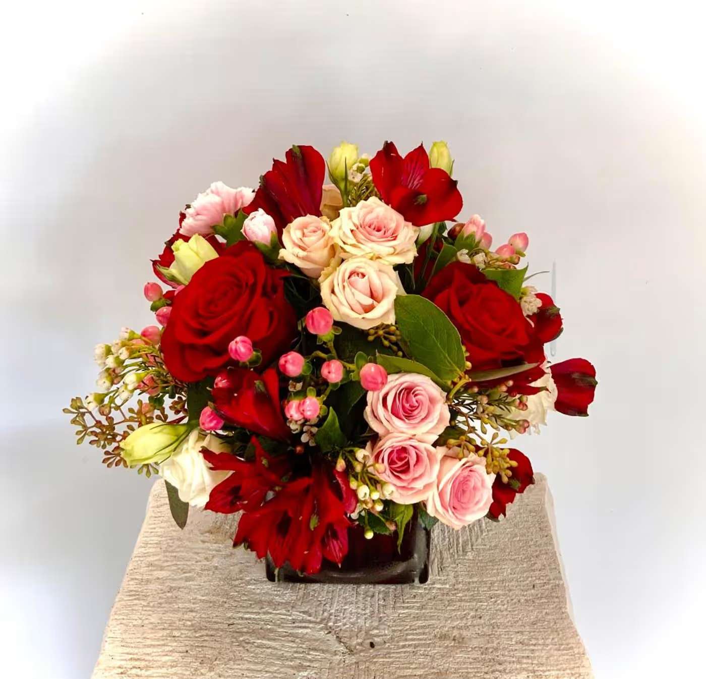 Bouquet of red and pink roses with red blooms in a dark vase