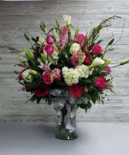 Pink and white floral arrangement in a glass vase with a checkered ribbon