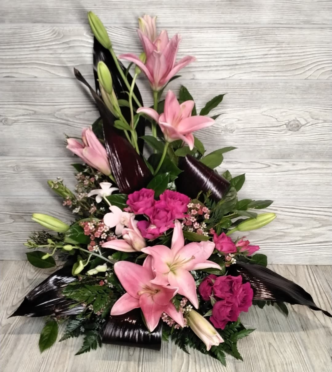 Pink lilies and magenta flowers in a low arrangement with dark leaves