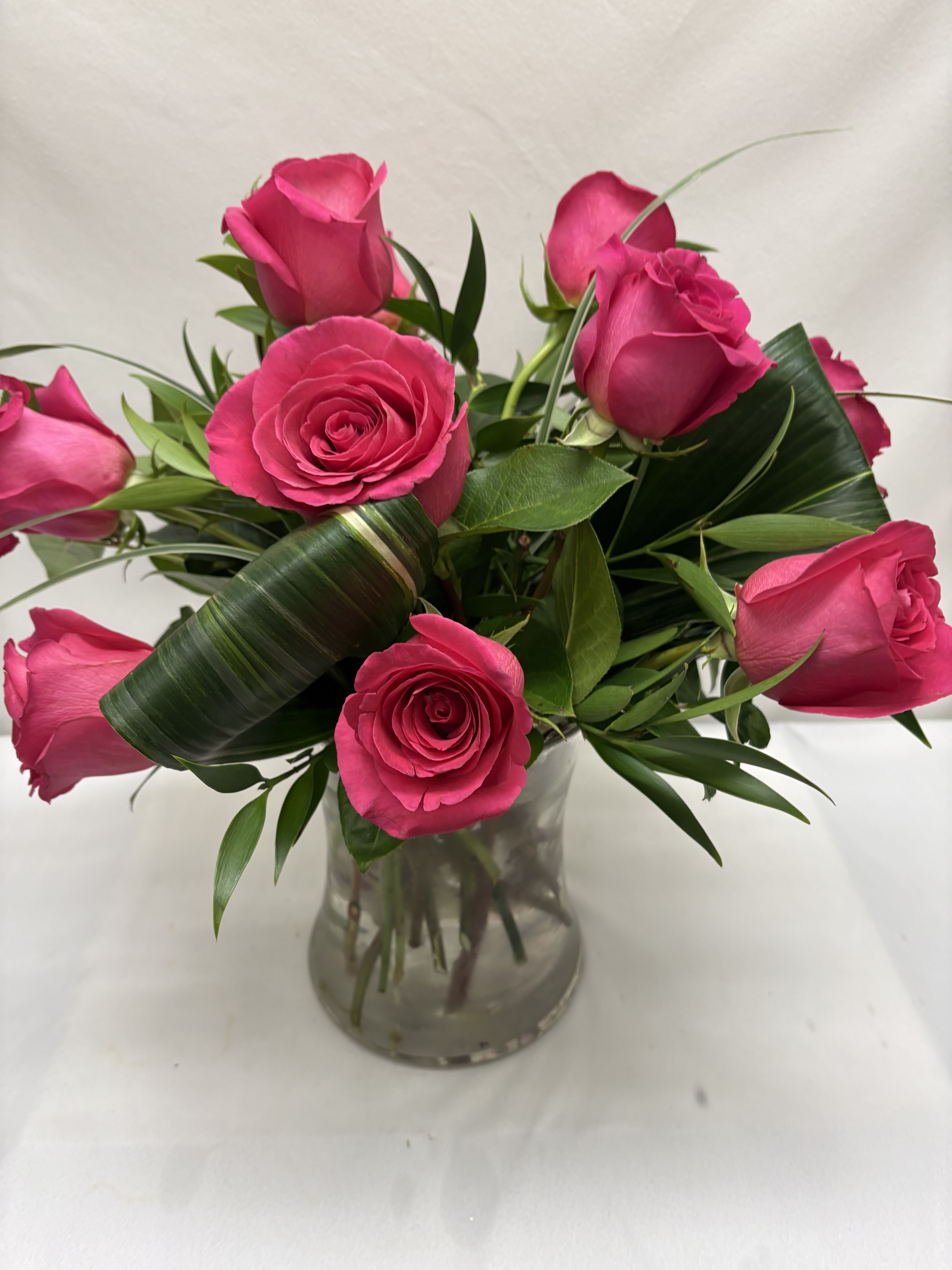 Short arrangement of hot pink roses with looped green leaves in a clear glass vase.