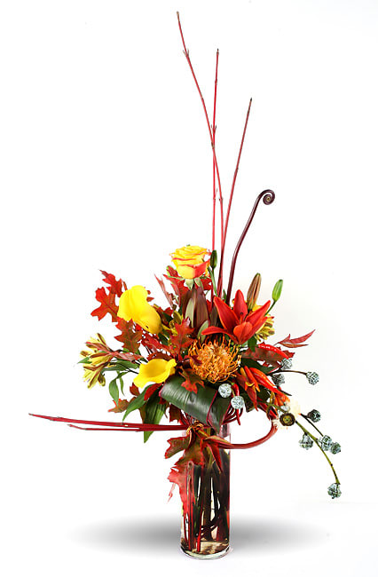 Tall autumn bouquet with yellow roses and orange lilies in a glass vase