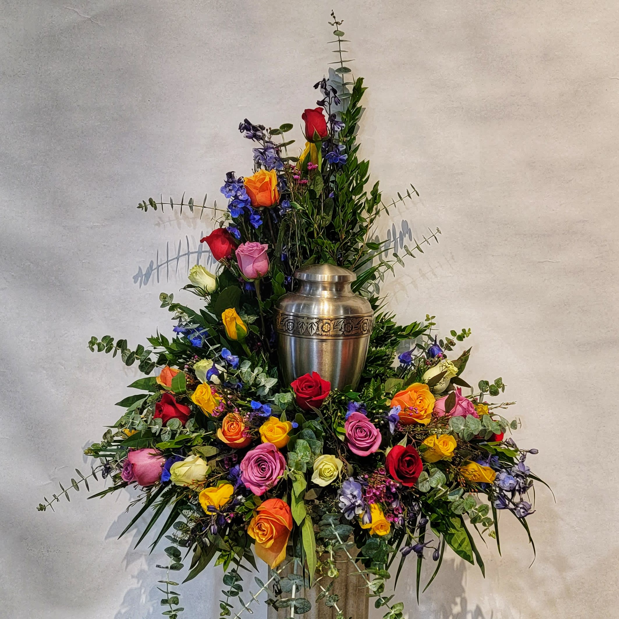 Tall floral arrangement with multicolored roses around a silver urn