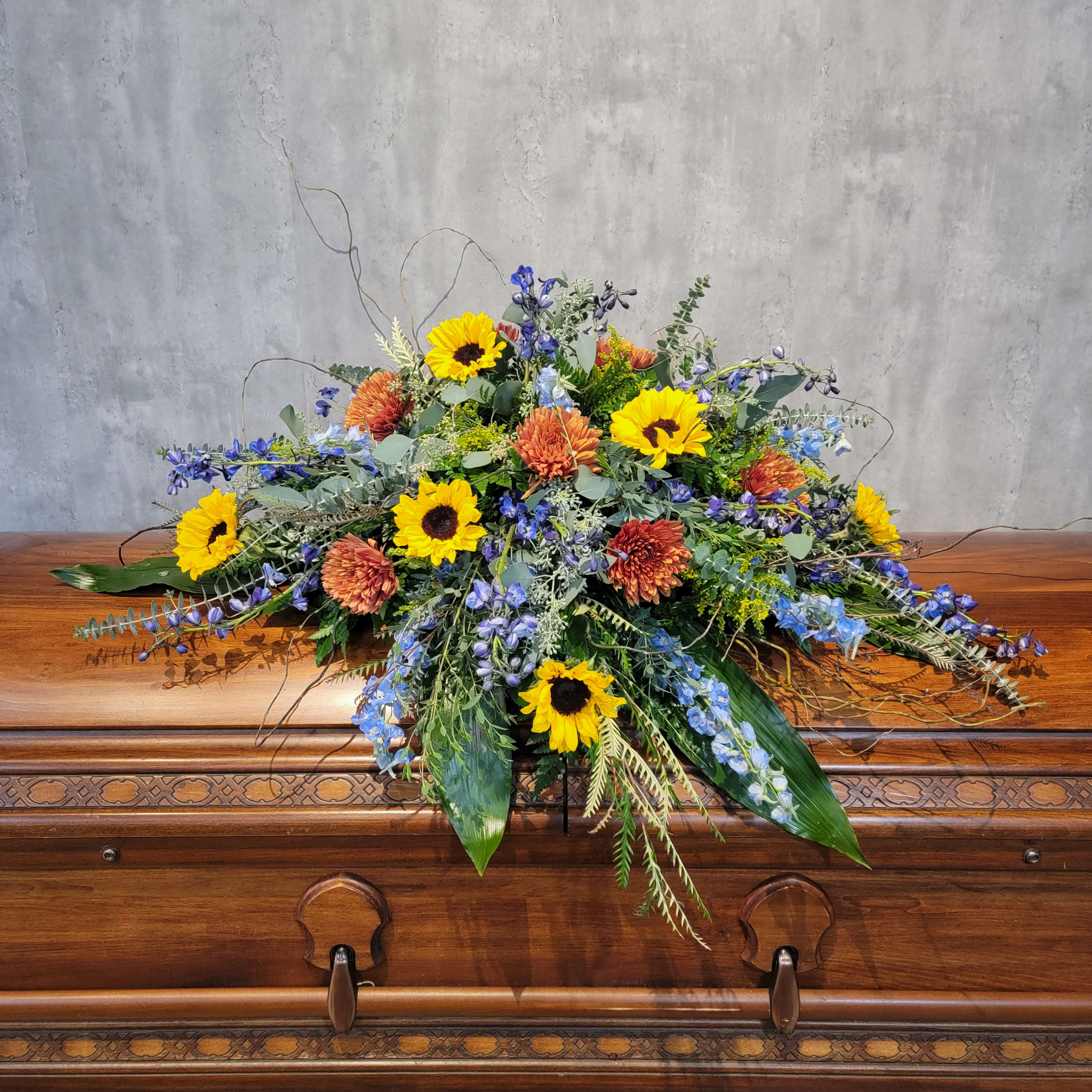 Large floral spray with sunflowers and orange blooms on a casket