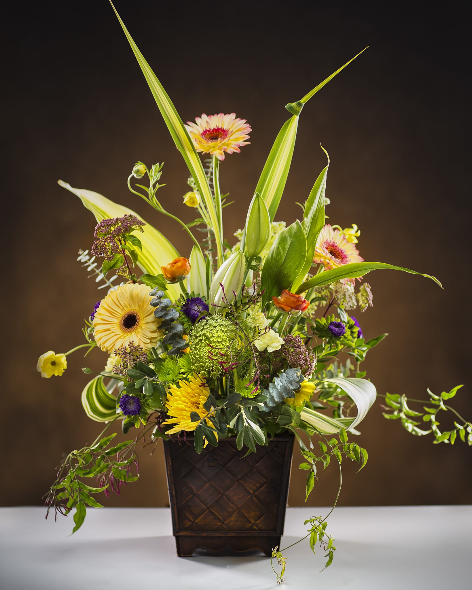 Tall mixed flower arrangement in a dark square vase