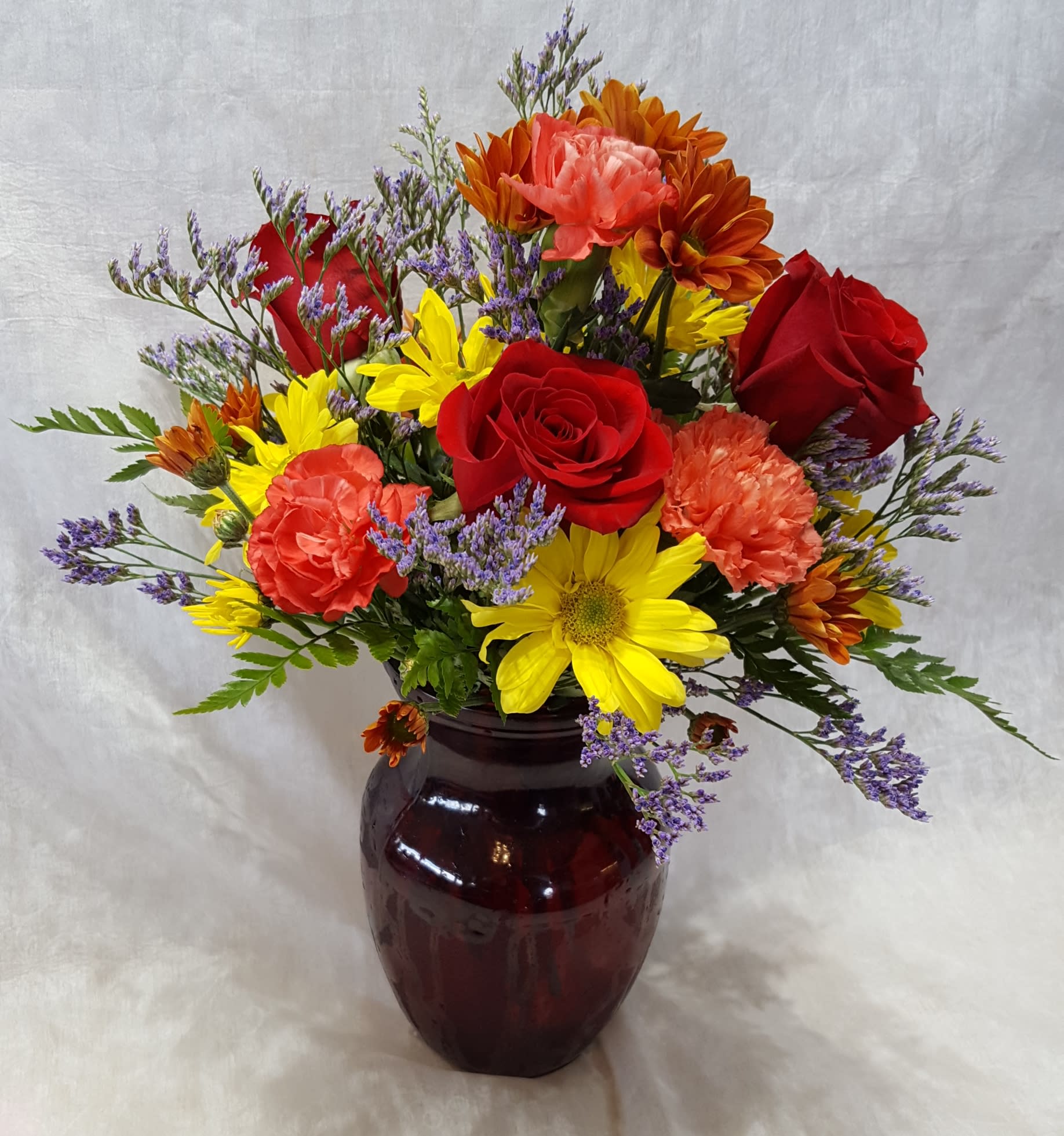 Autumn Boldly Bashful - This bouquet is a sweetly demure way to show someone you care.   Arrangement Details: Includes fall chrysanthemums spray daisies, orange carnations, and red roses in a clear vase. COLORS WILL VARY WITH AVAILIBILTY.  APPROXIMATE DIMENSIONS: 12" H X 10" W