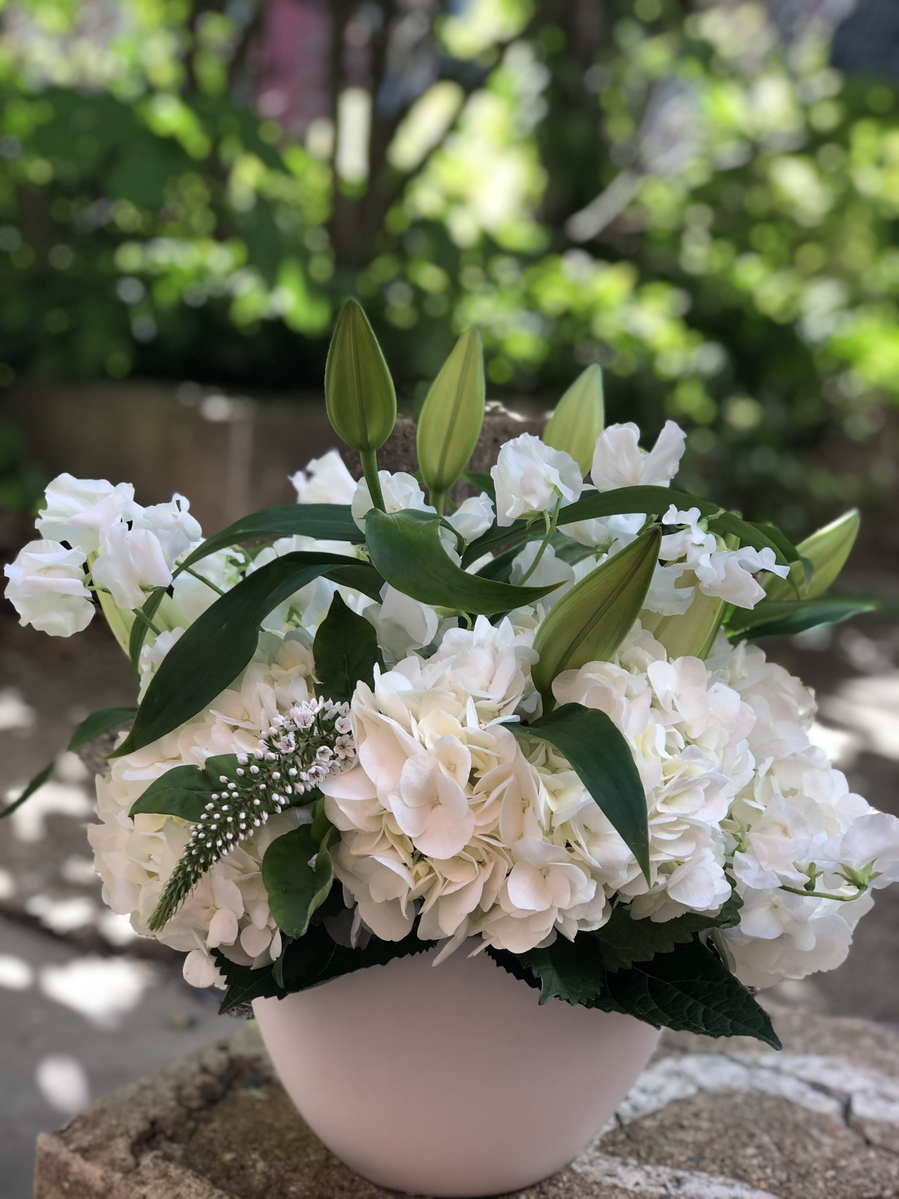 White floral arrangement with lilies and hydrangeas in a pale vase