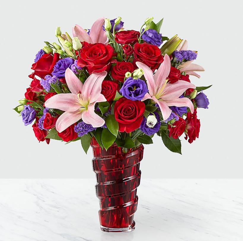 Bouquet of red roses, pink lilies, and purple flowers in a red glass vase