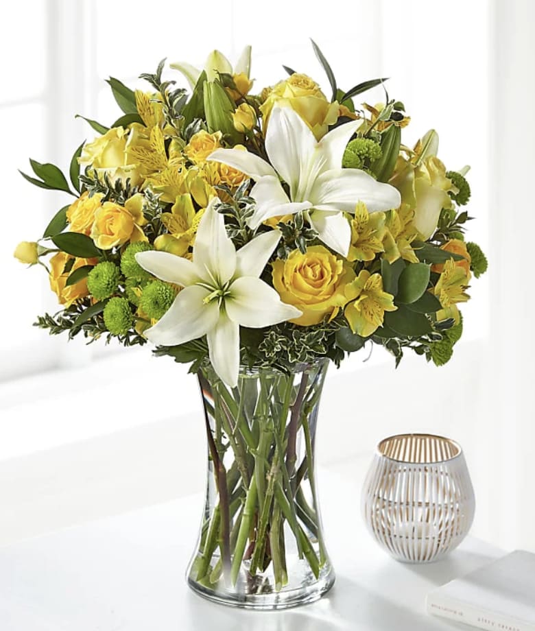 Yellow roses and white lilies arranged in a clear glass vase