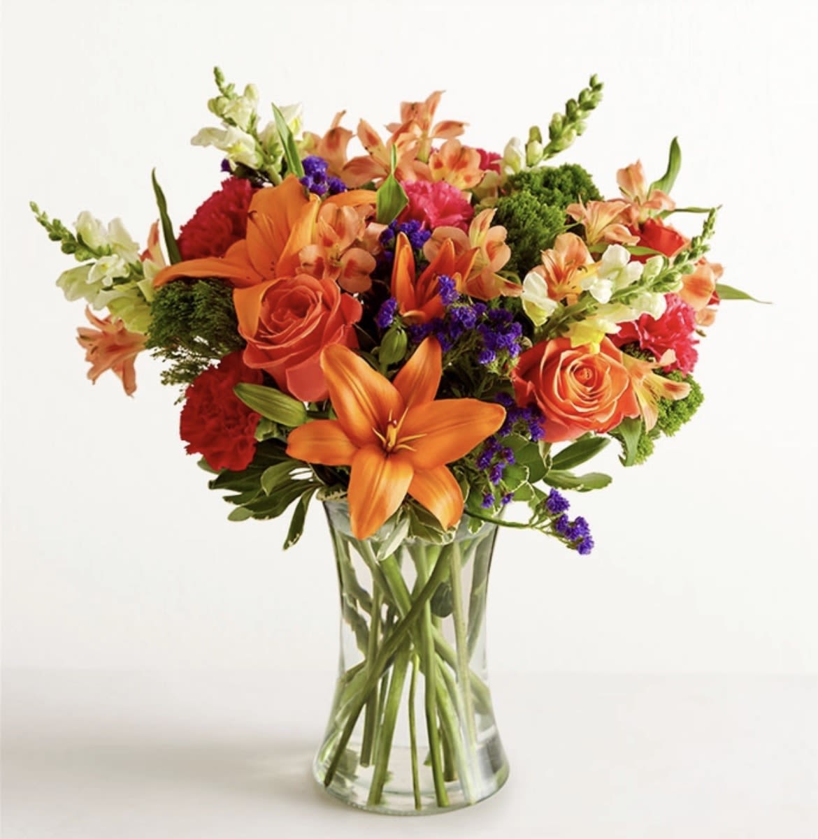 Mixed bouquet of orange and red flowers in a clear glass vase