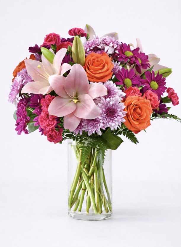 Mixed pink, purple, and orange flowers in a clear glass vase