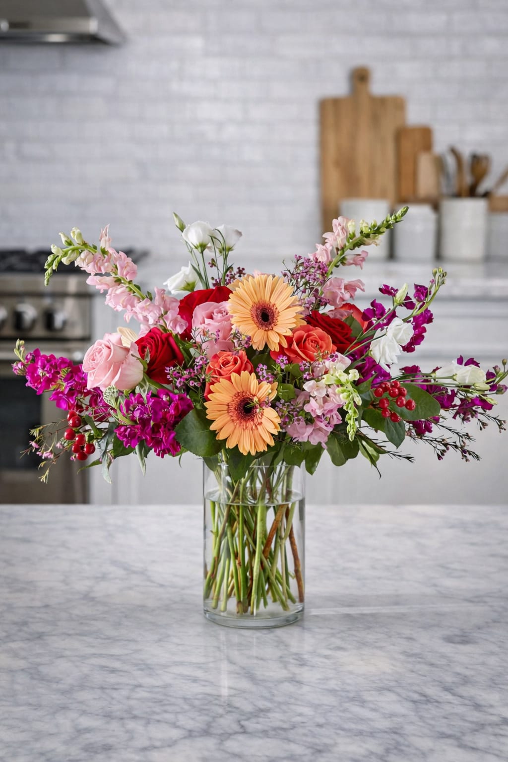 Mixed bouquet of roses, gerbera daisies, and pink blooms in a clear glass vase