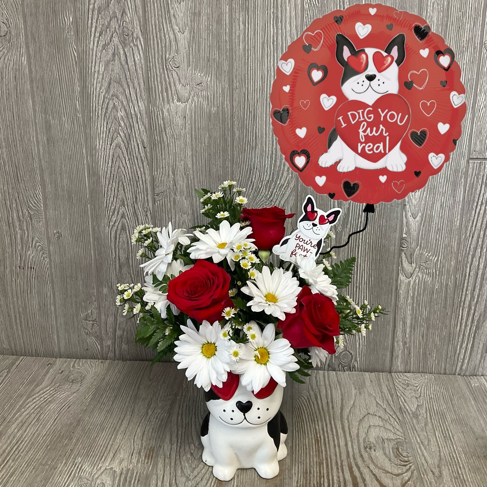 Red roses and white daisies in a dog-shaped vase with a heart balloon.