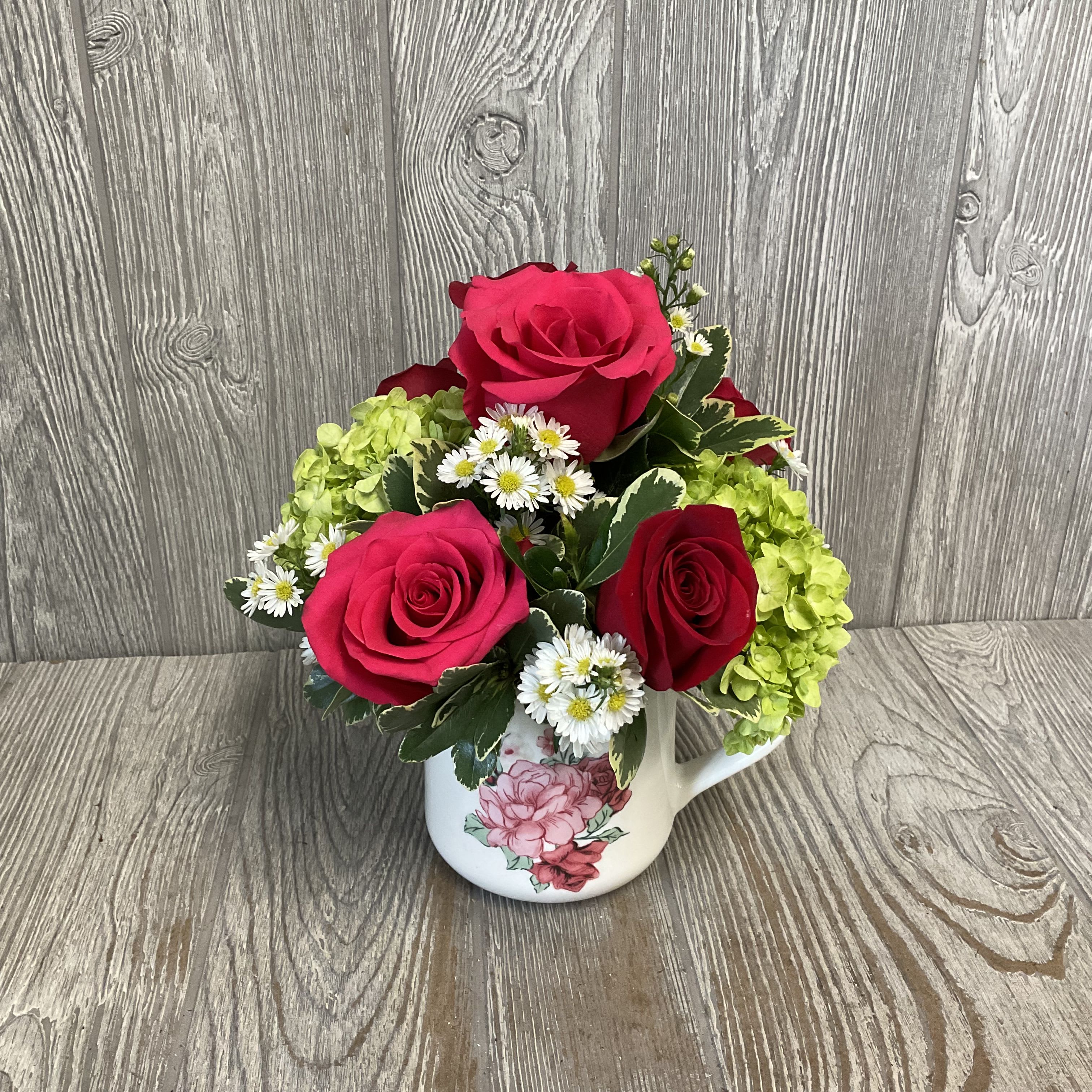 Pink and red roses with white daisies in a floral mug