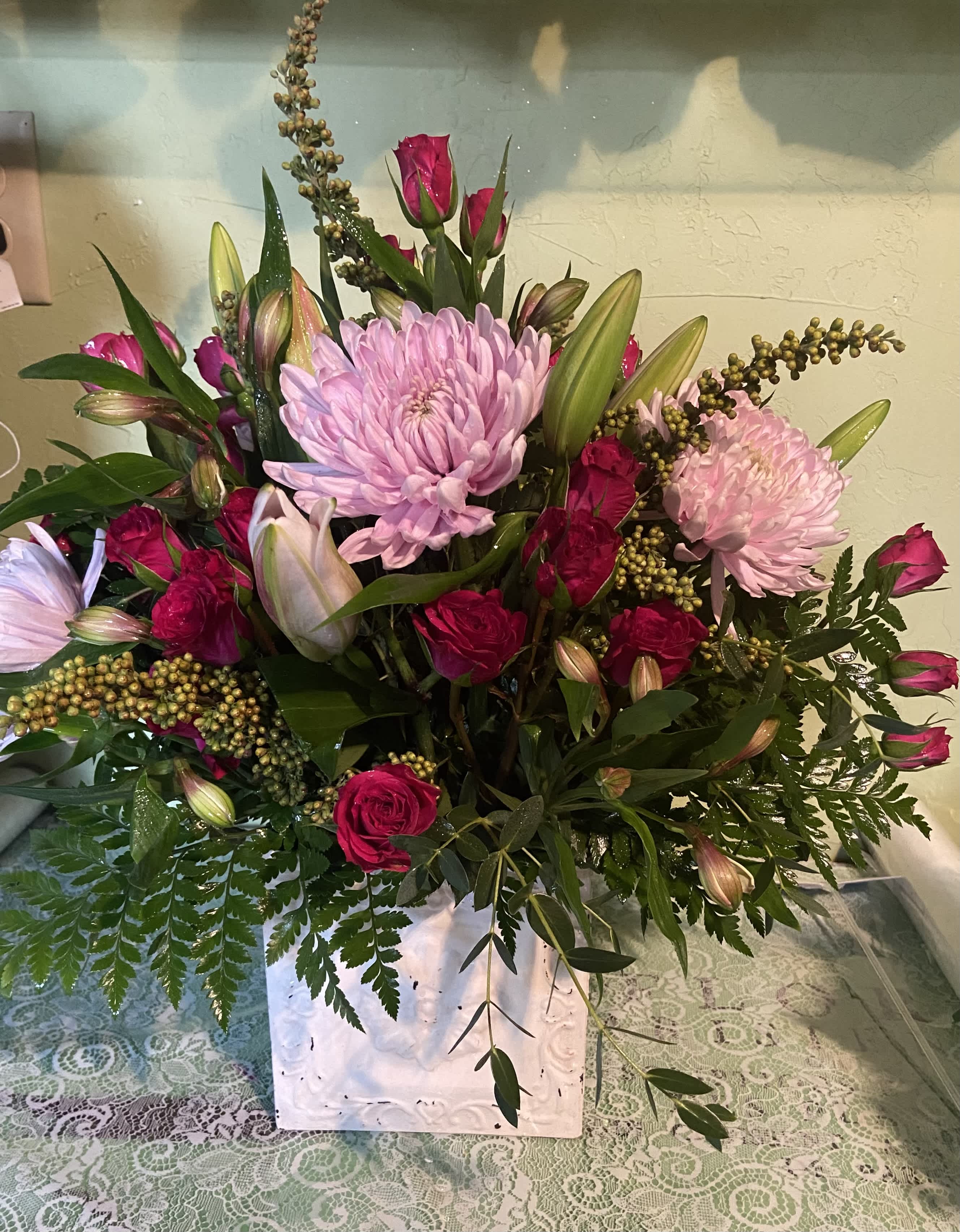 Pink roses and lilies arranged with large pink chrysanthemums in a white vase