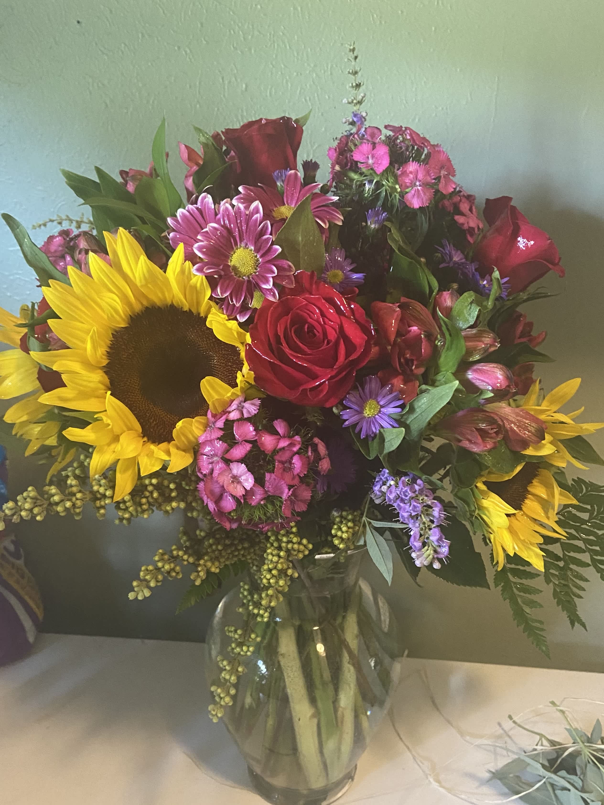 Bouquet of sunflowers, red roses, and pink mixed flowers in a glass vase
