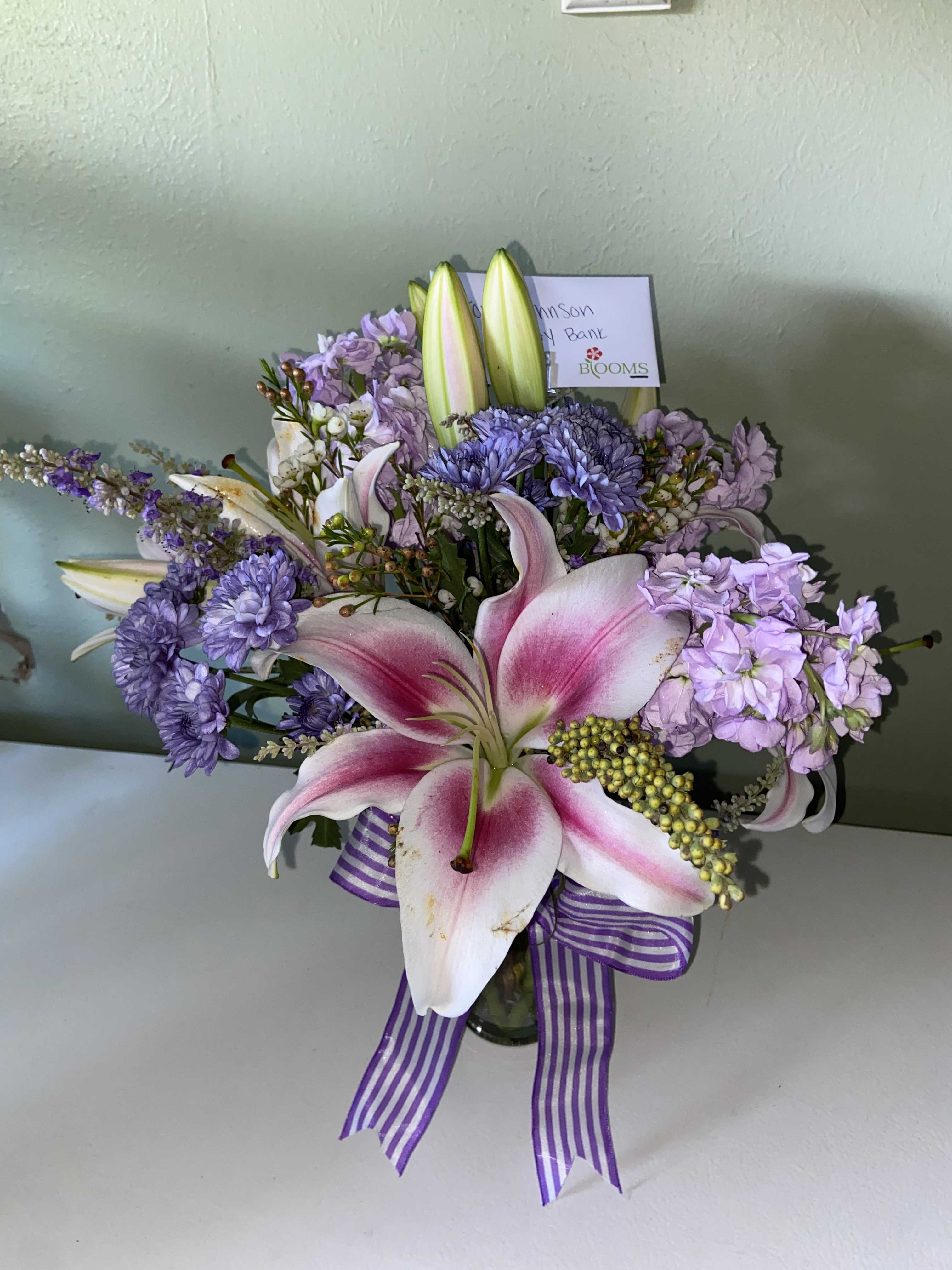 Pink lilies and lavender flowers in a glass vase with a striped ribbon
