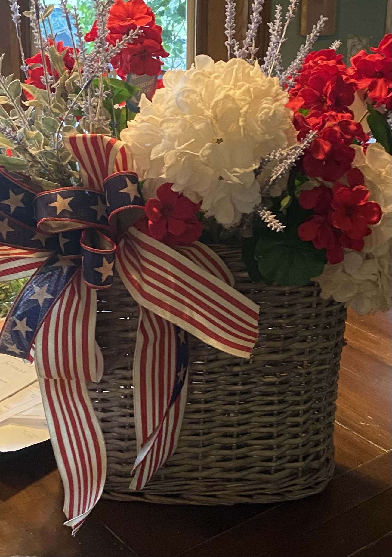 Red and white floral arrangement in a woven basket with an American flag ribbon