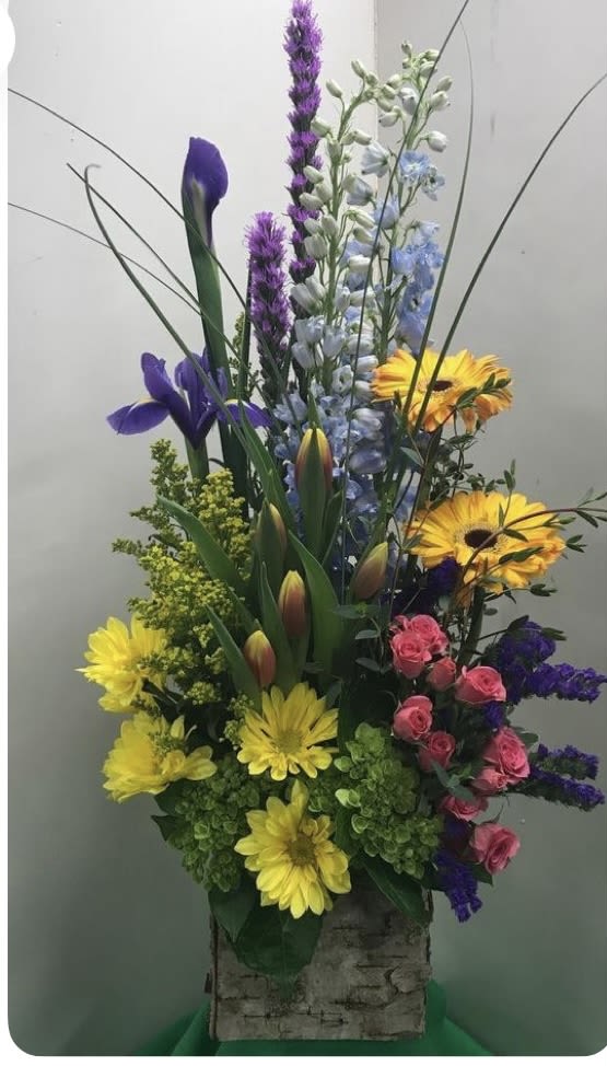 Tall mixed flower arrangement in a birch bark container with yellow, purple, pink, and blue blooms