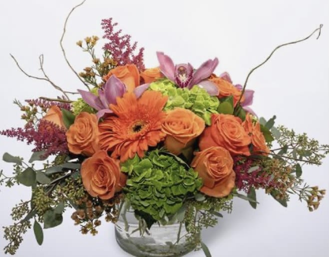 Orange roses and gerbera daisies in a glass vase with purple accents