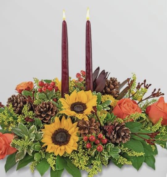 Autumn floral centerpiece with sunflowers, roses, pinecones, and two burgundy candles
