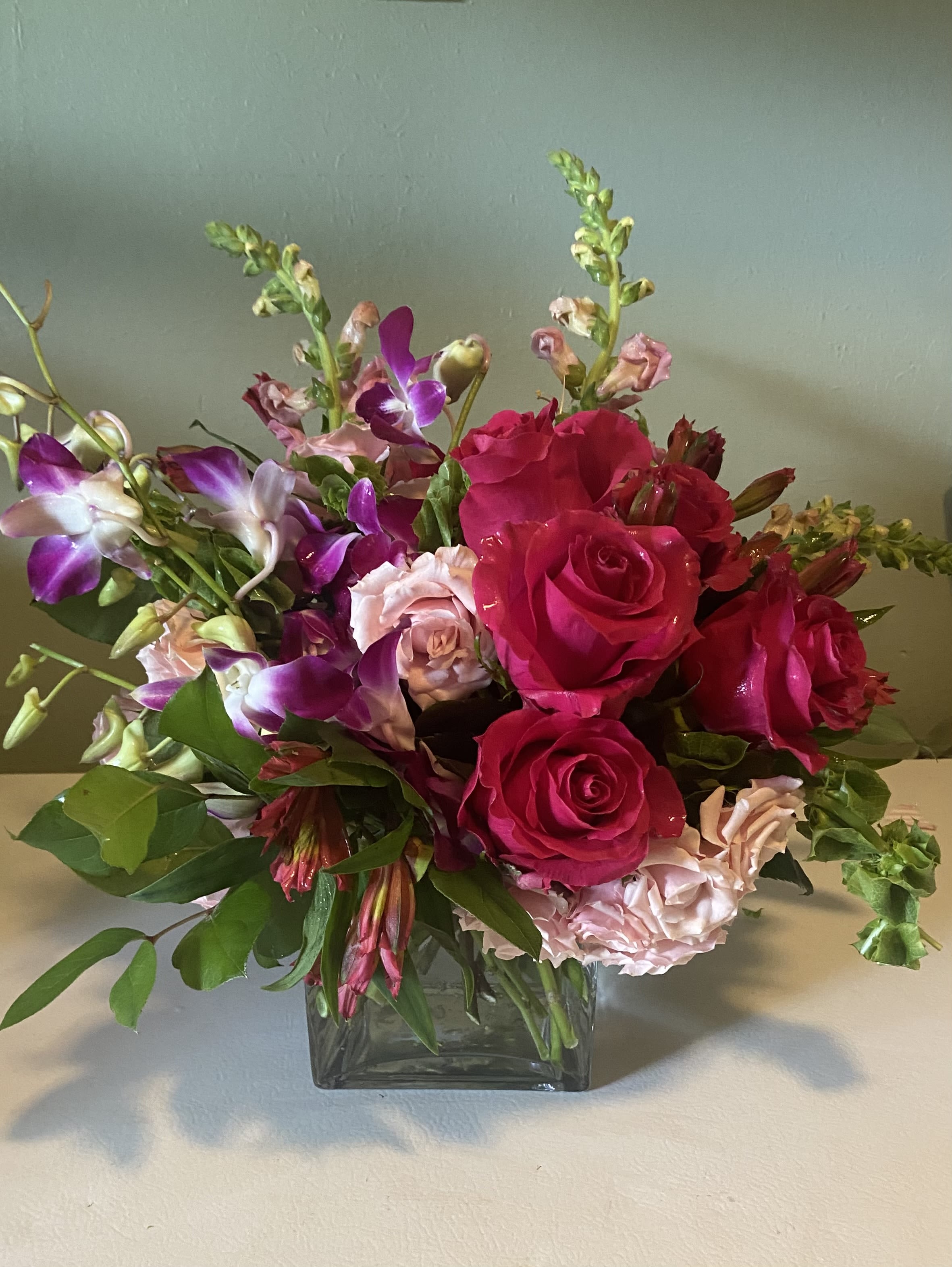 Pink roses and purple orchids arranged in a square glass vase