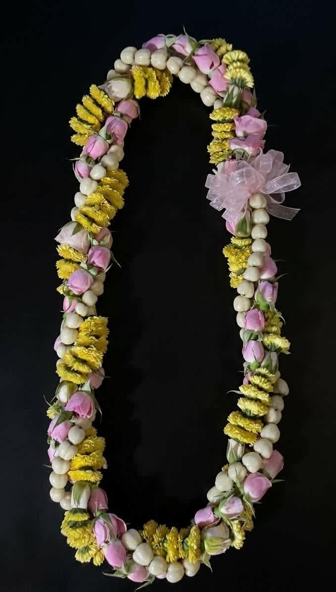 Floral lei with pink buds, yellow flowers, and white beads on a black background