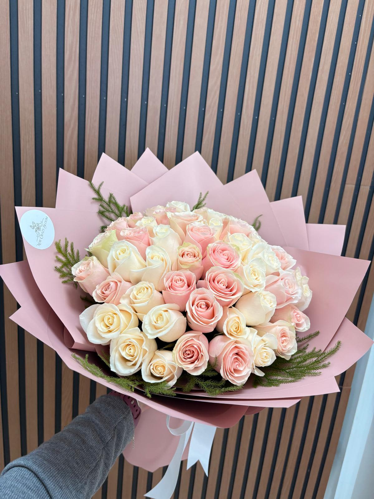 100 Pink MIX roses  - A lavish cascade of soft pink, cream and pale yellow roses-this large rose bouquet reads like a love letter in bloom and is perfect for an anniversary, Mother's Day, or any moment when you want someone to feel deeply cherished. The dense, abundant arrangement presents one hundred roses in a lush, full dome that announces celebration without saying a word, making it equally fitting for birthdays, graduations, weddings, or a grand "I'm sorry" or "Thank you."  Each bloom is layered into a tightly packed bouquet and wrapped in pastel decorative paper, finished with a dark ribbon printed with "LOVE YOU" for a personal, romantic touch. The color palette feels fresh for spring and summer yet gentle enough for autumn and winter occasions; sizes are generous and meant to be a centerpiece-worthy gift. Ideal for sending to a partner, parent, new baby family, or friend who deserves to feel truly seen-place your order early for holidays, graduations, or Mother's Day to ensure timely delivery.