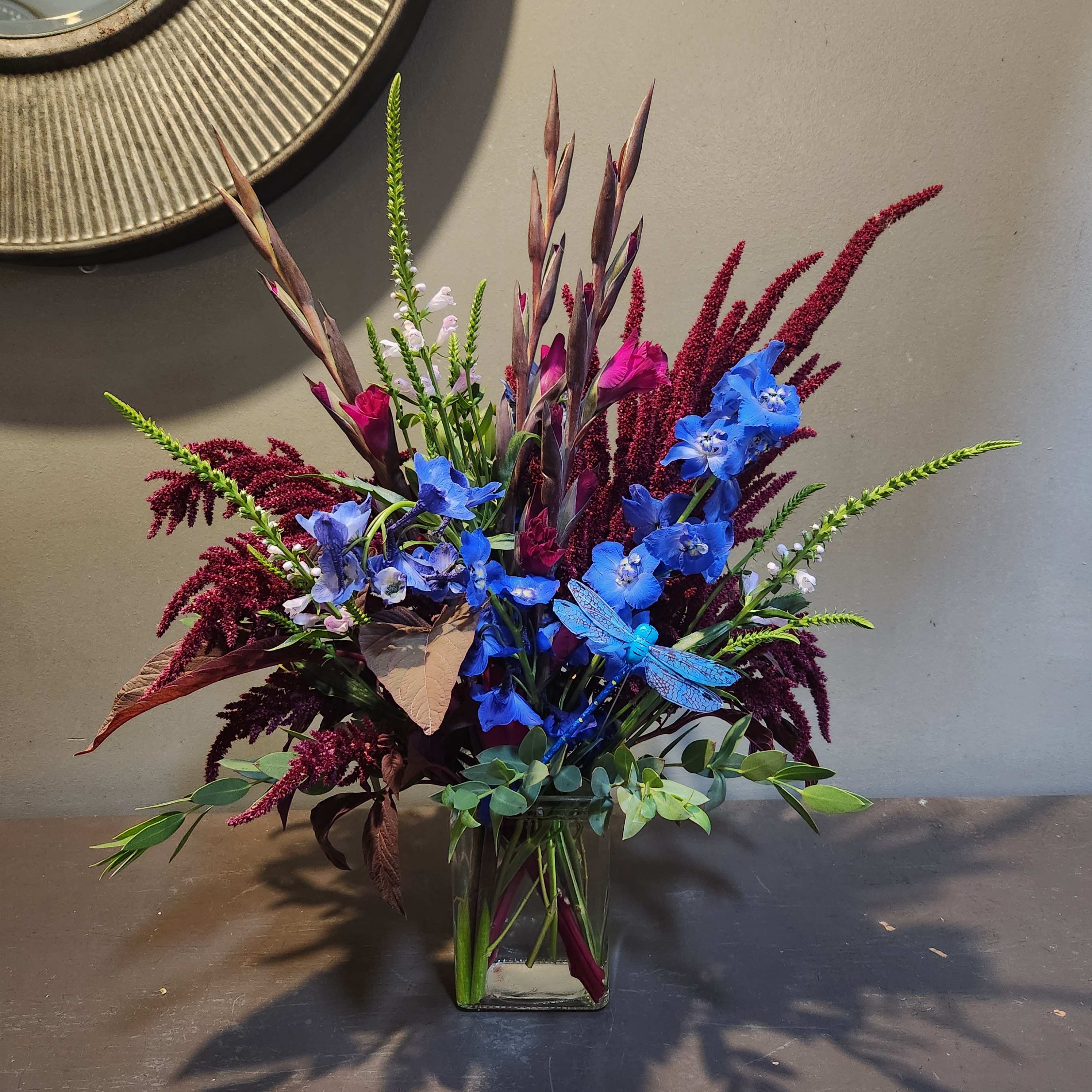Blue and burgundy floral arrangement in a clear glass vase