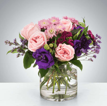 Coming Home by BloomNation™ - A selection of pink and purple flowers come together in an eye-pleasing arrangement. This arrangement makes a great gift for Mother's Day, Women's Day, or as a thinking of you present.  Approximate Dimensions: 10''D x 10''H