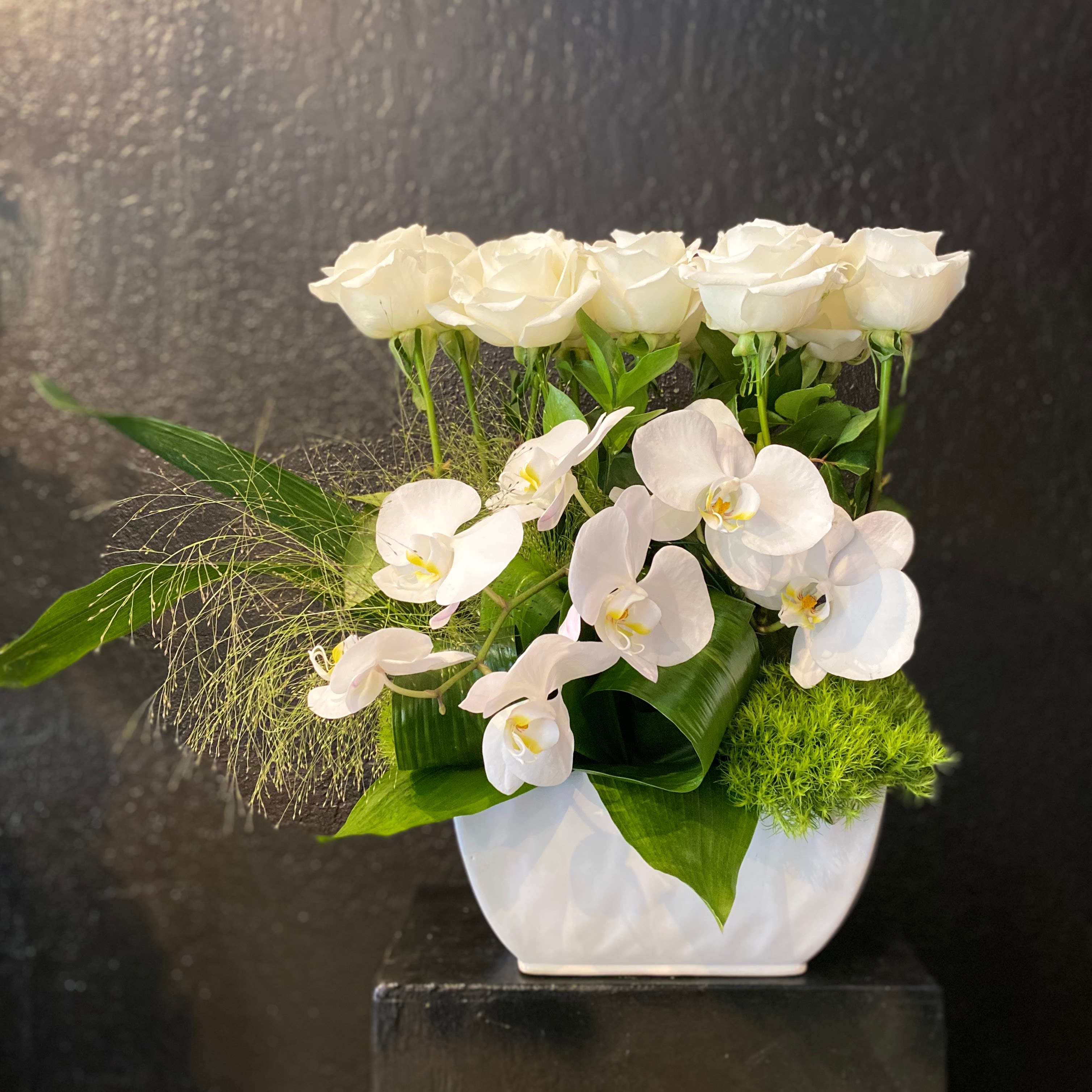 Modern white arrangement of roses and orchids in a white vase with bold green accents.