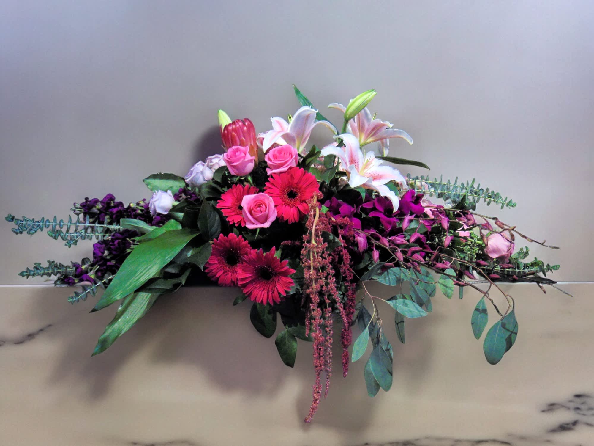 Long low arrangement with pink gerbera daisies, roses, lilies and purple blooms