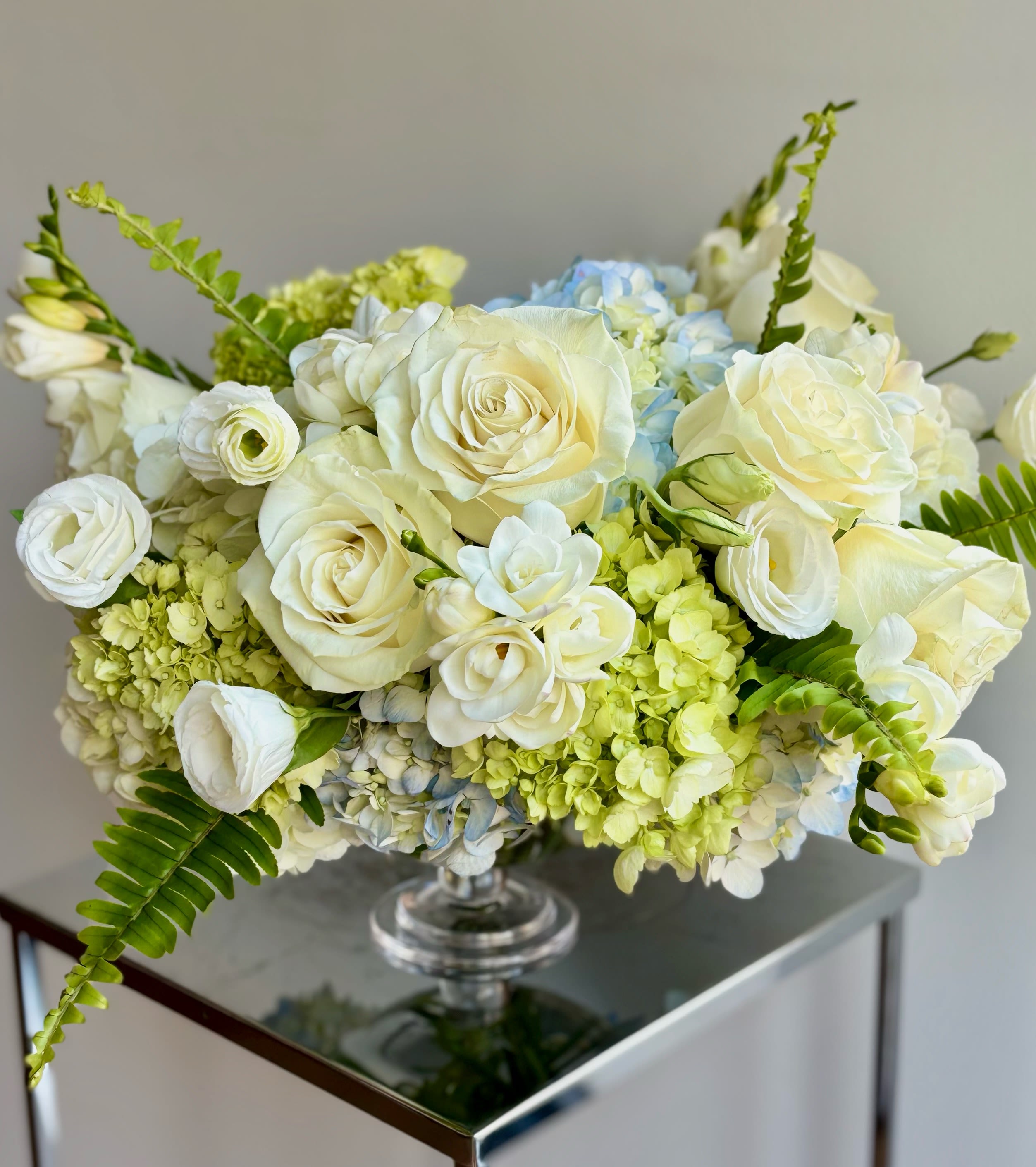 White roses and pale blue hydrangeas in a clear glass vase